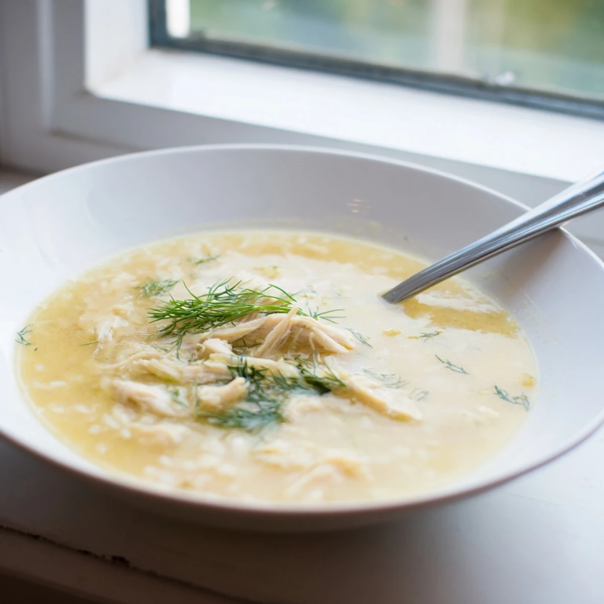 Homemade avgolemono Greek lemon chicken soup showcasing silky egg-lemon broth with succulent chicken pieces and white rice