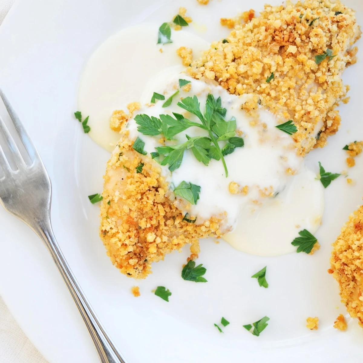Golden brown Parmesan crusted chicken breast drizzled with rich creamy garlic sauce on white plate