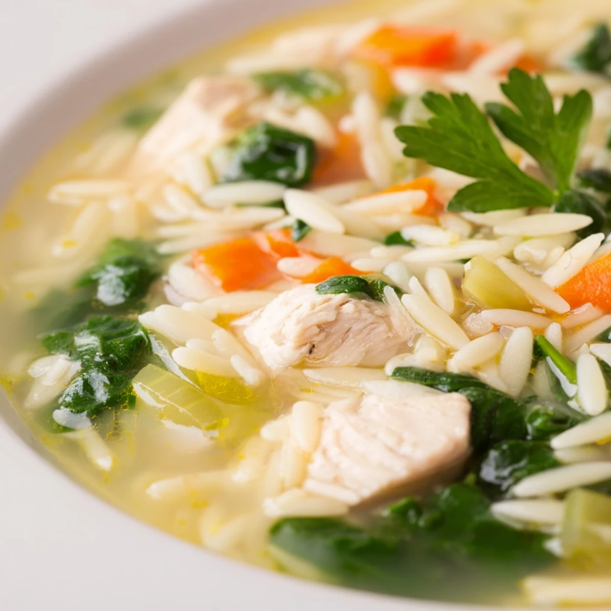 Golden chicken pieces swimming in spring lemon chicken orzo soup with fresh spinach and orzo pasta in a rustic bowl