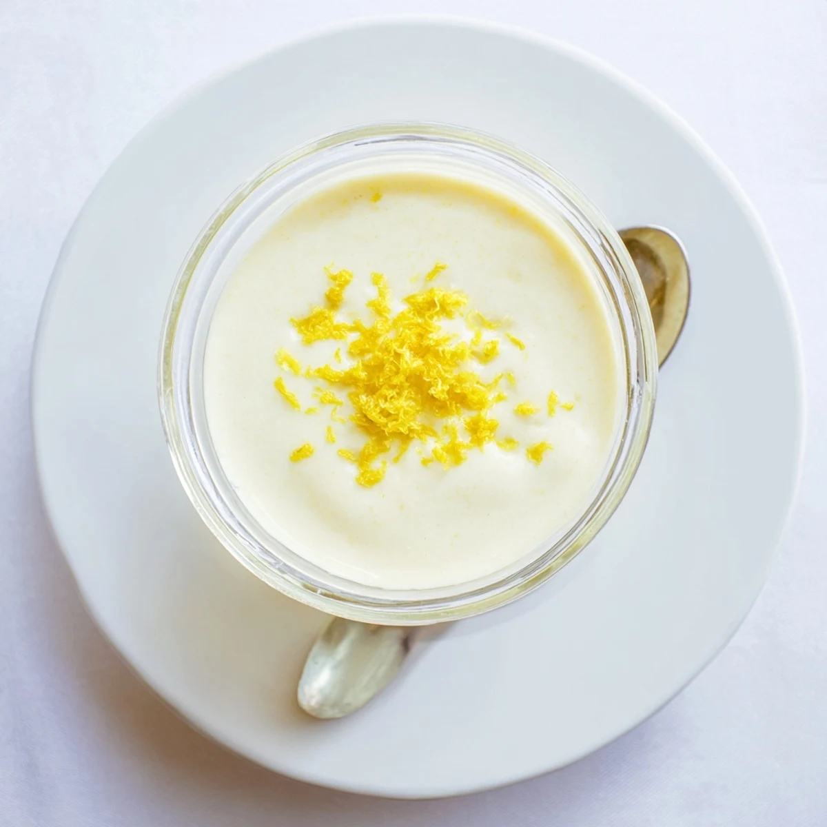 Creamy lemon posset dessert in individual ramekin topped with bright yellow zest and mint leaf