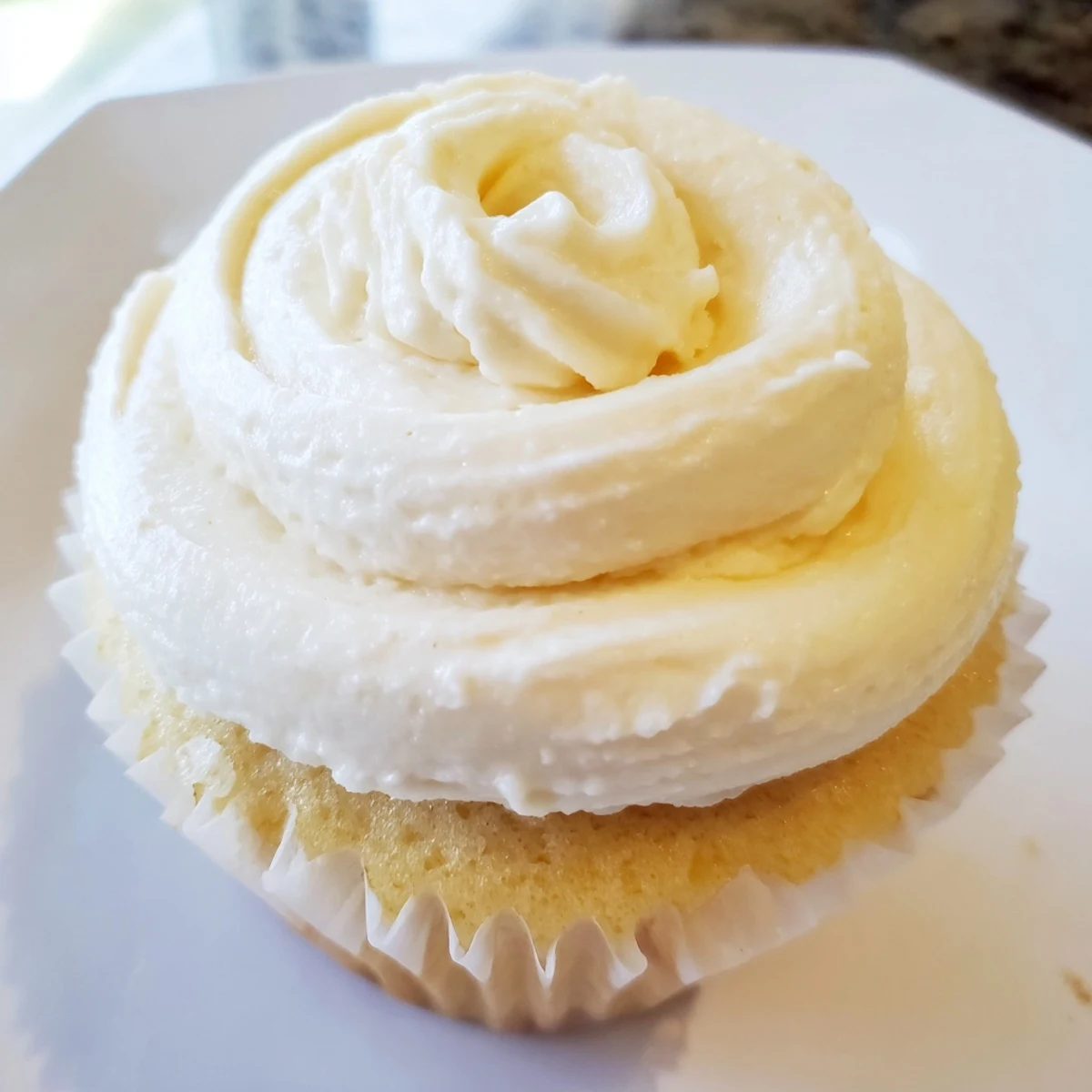 Fluffy vanilla cupcakes topped with creamy white buttercream frosting on a white plate