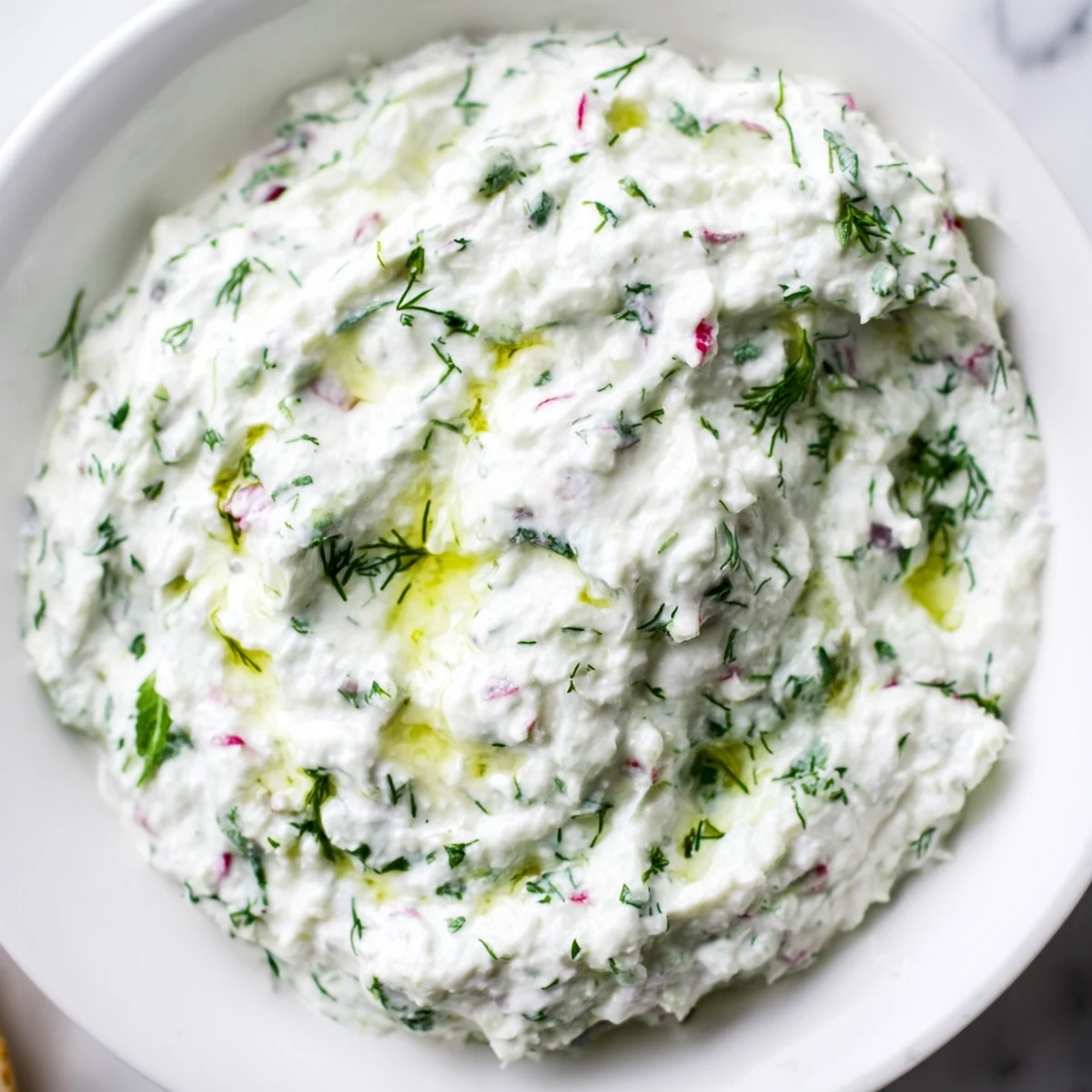 Creamy healthy radish tzatziki dip topped with fresh dill and a drizzle of olive oil