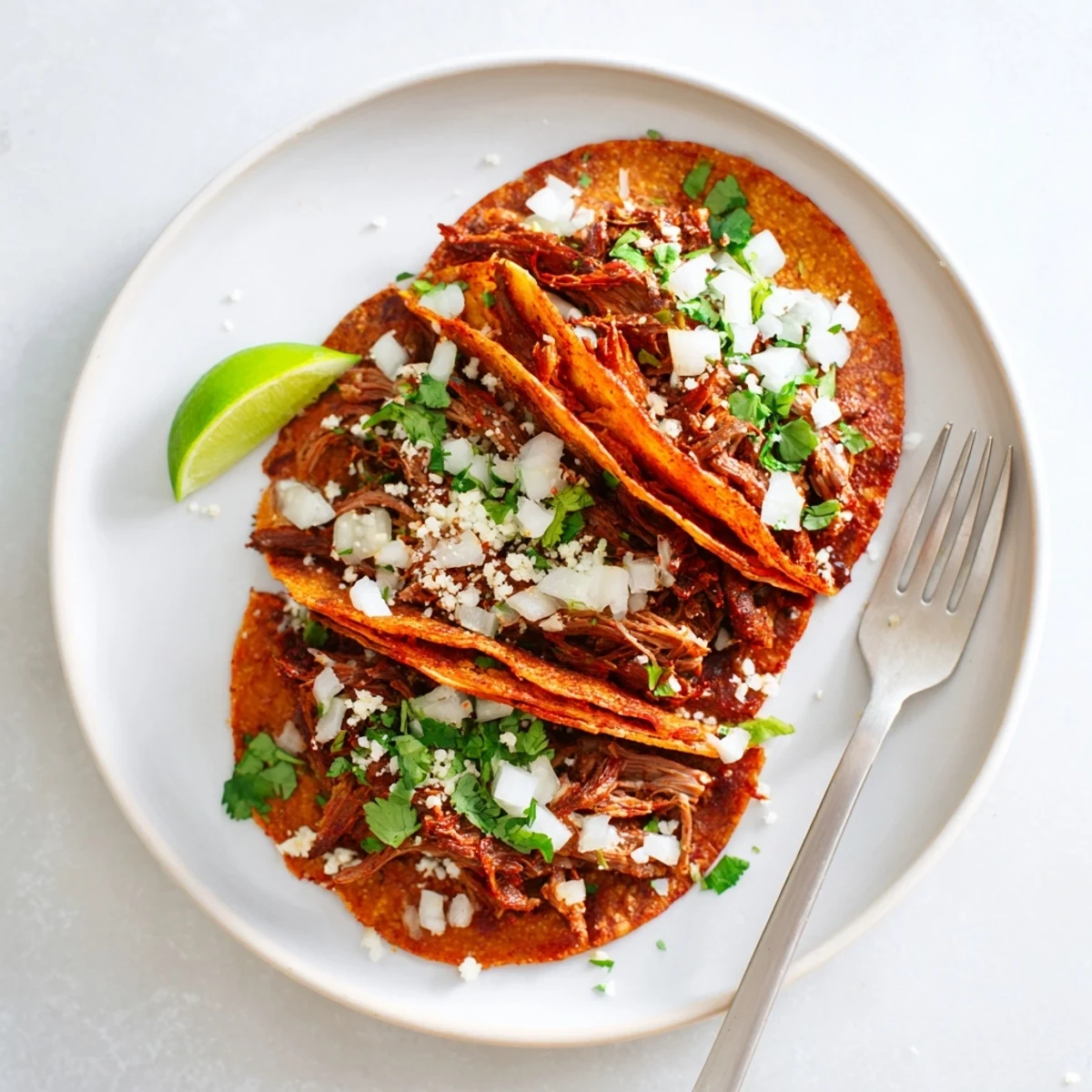 Slow cooker birria tacos oozing melted cheese with a warm bowl of spiced broth for dipping
