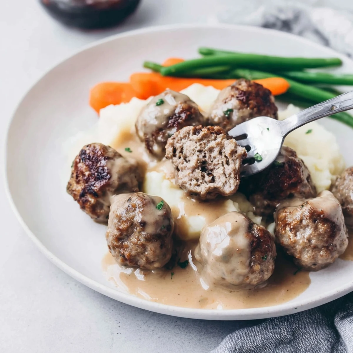Homemade Ikea Meatballs glistening in creamy gravy, browned edges, steaming over mashed potatoes