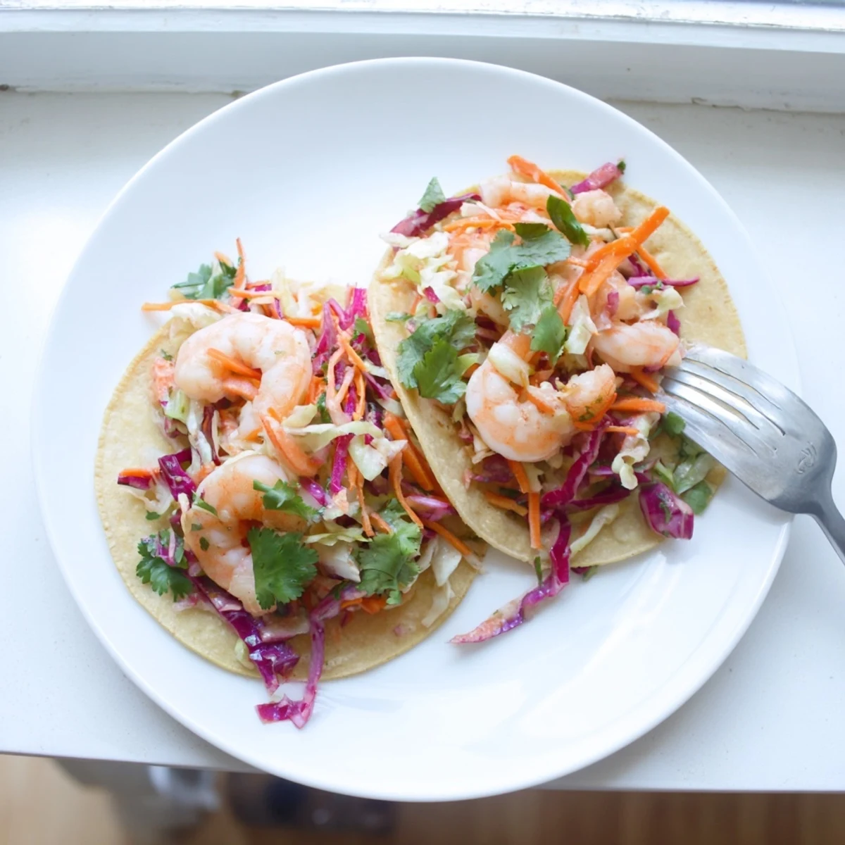Golden seasoned shrimp tacos topped with colorful purple and green cabbage slaw in warm tortillas