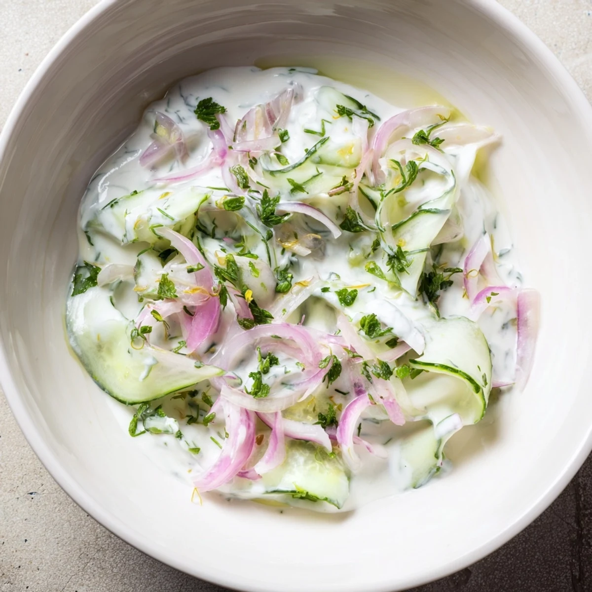 Creamy Greek yogurt cucumber salad chilled in a white bowl topped with fresh dill and thinly sliced red onions.