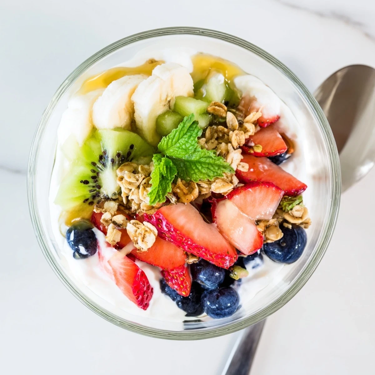 Creamy yogurt parfait recipe topped with colorful strawberries, blueberries, and sweet honey drizzle