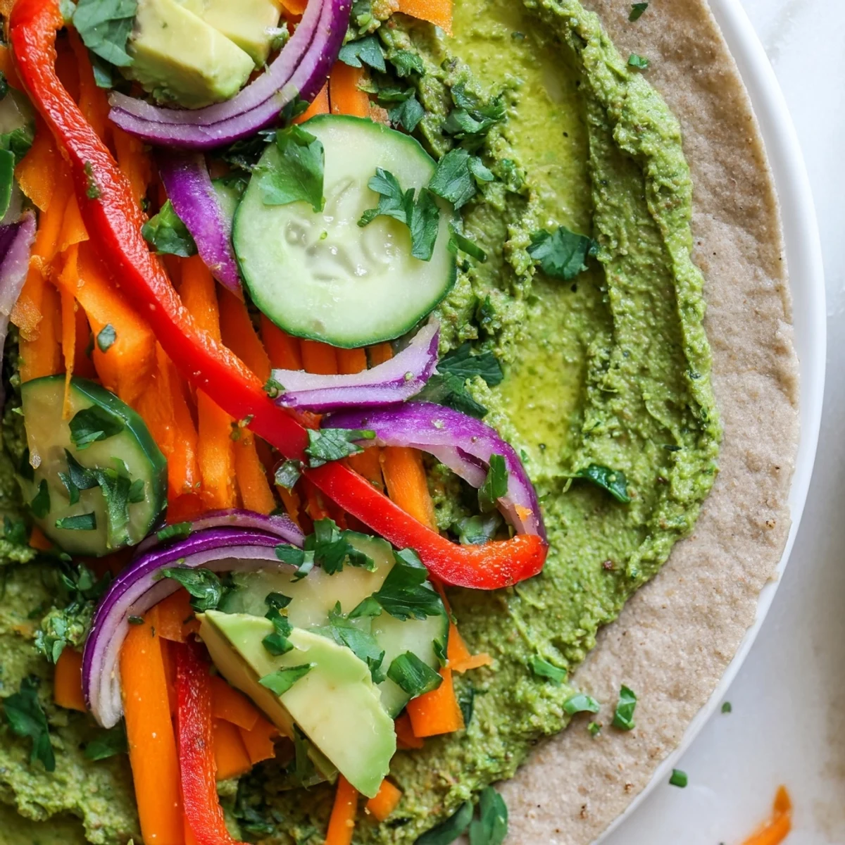 Cross-section of Mediterranean lunch wrap revealing creamy spinach hummus layered with fresh carrots peppers avocado