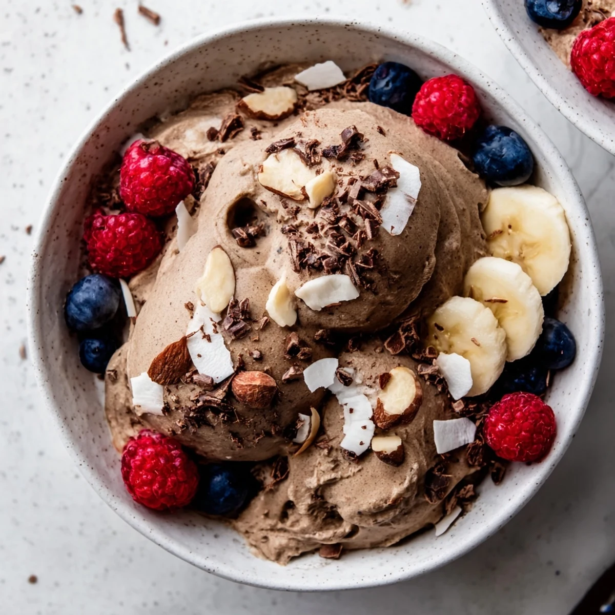 Creamy healthy nice cream served in bowls topped with fresh berries and dark chocolate shavings