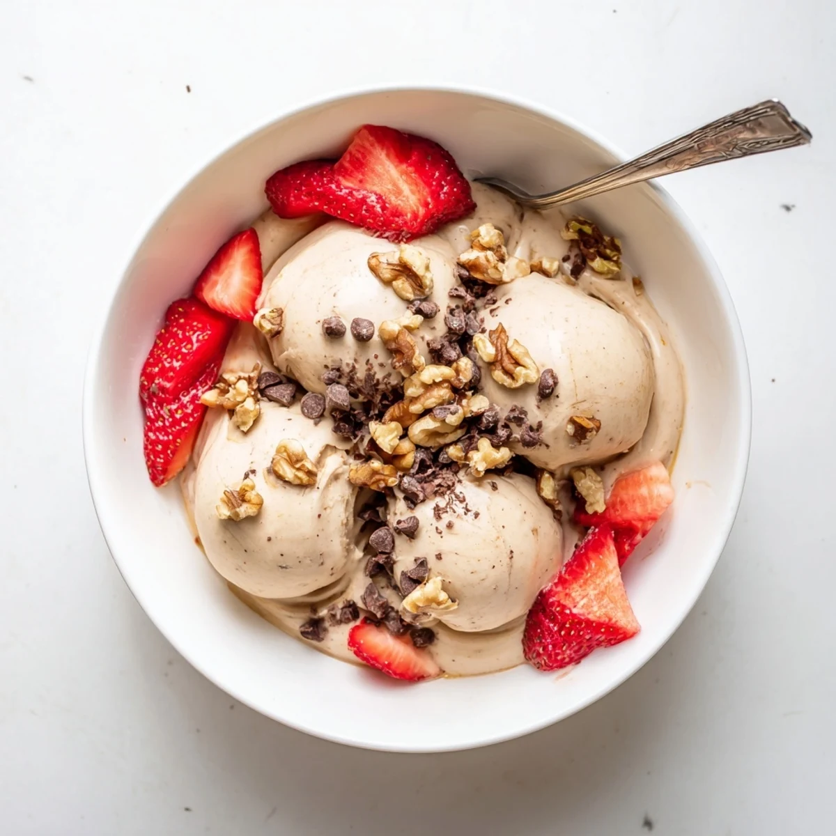 Creamy banana nice cream served in a bowl topped with fresh berries and chopped nuts