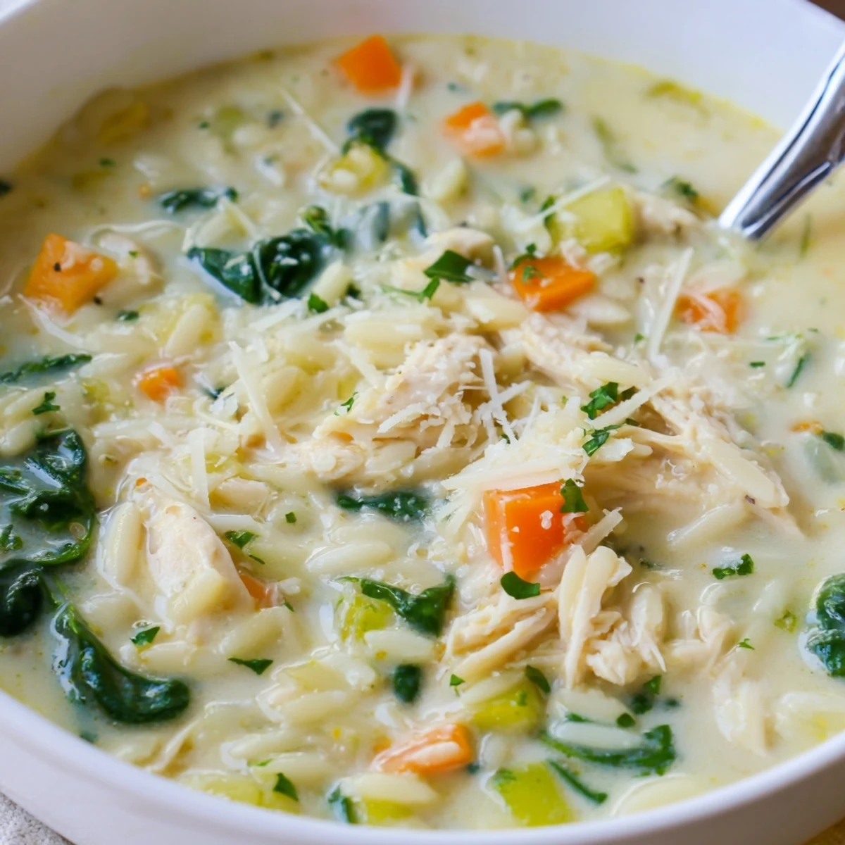 Spoon lifting Creamy Chicken Florentine Soup With Orzo, tender chicken, wilted spinach  
