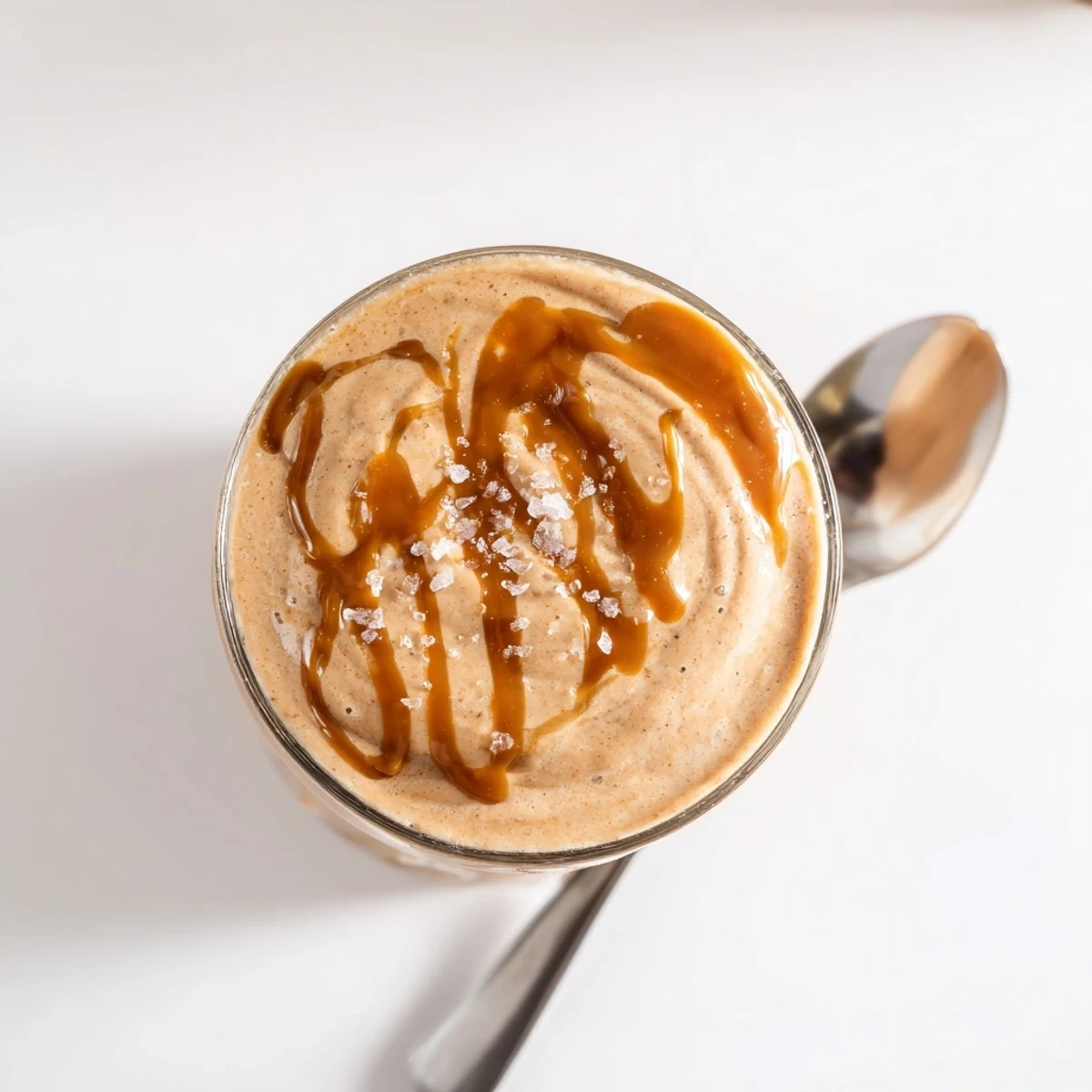 Thick salted caramel protein smoothie poured into a glass with caramel drizzle down the sides