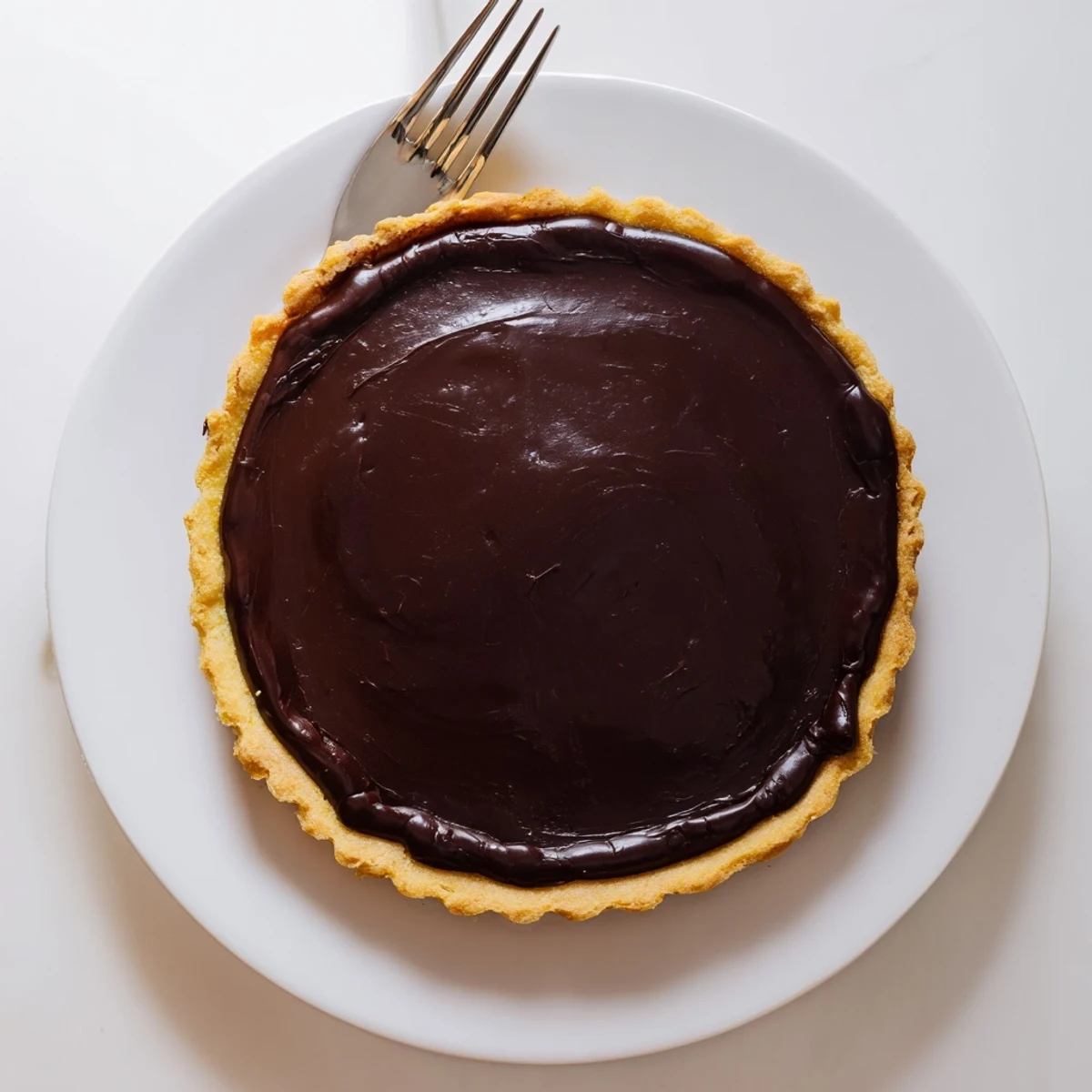 Slice of French chocolate flan showing glossy dark custard nestled inside flaky tart crust