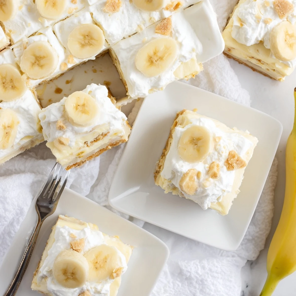 Golden banana pudding cheesecake squares layered with whipped cream and vanilla wafer crust