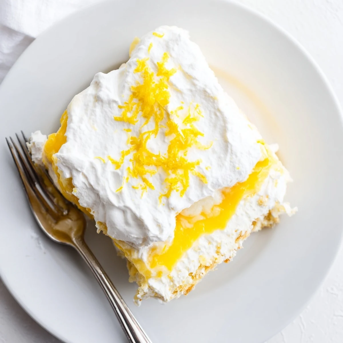 Golden slice of lemon lush cake with three distinct layers and creamy whipped topping