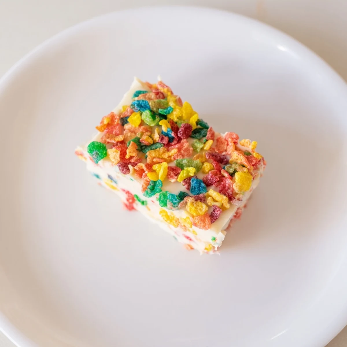 Colorful Fruity Pebbles cereal frosting piped onto a white cupcake with rainbow sprinkles