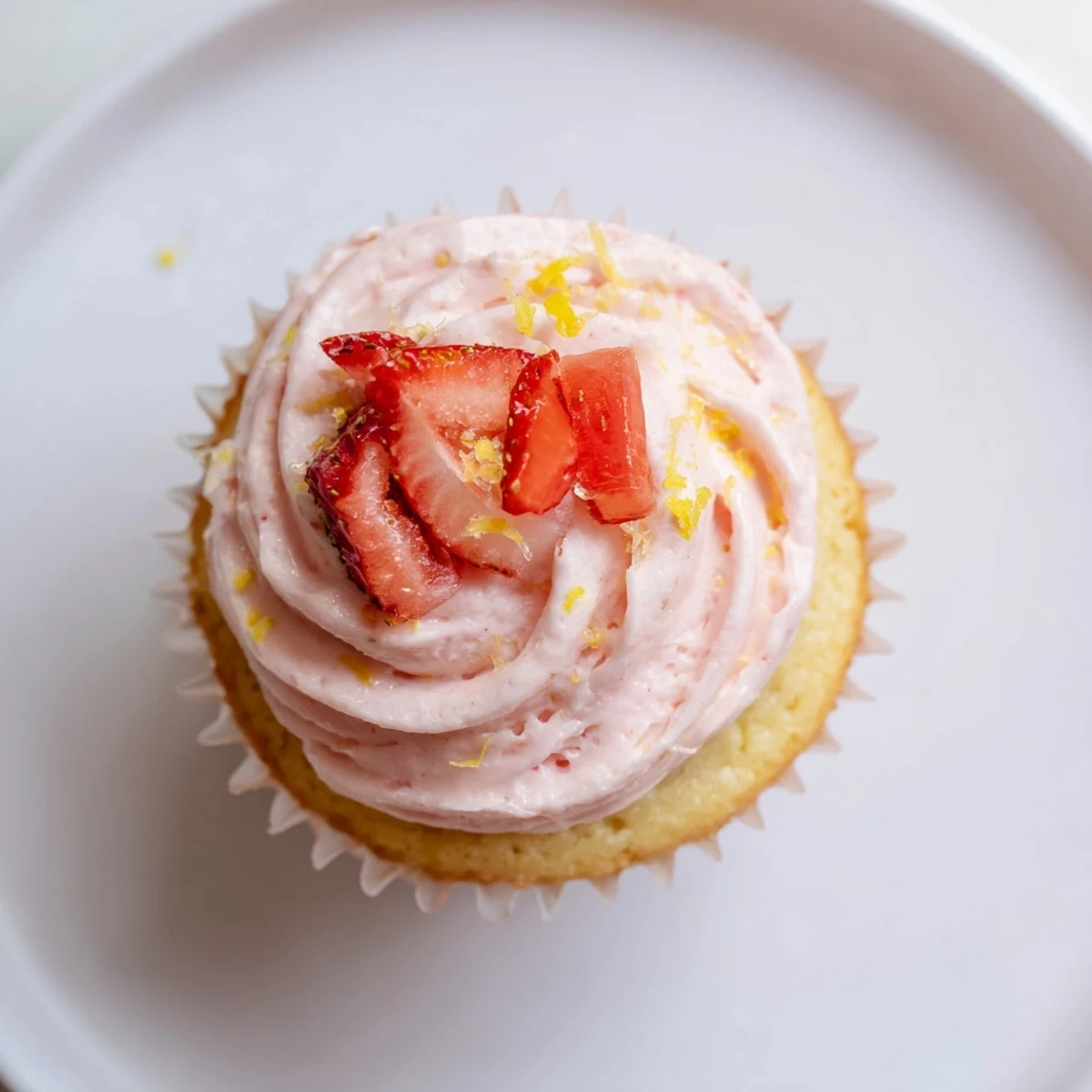 Pink frosted strawberry lemonade cupcakes with fresh strawberry slices and zest on serving plate