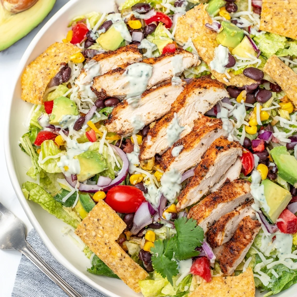 Colorful Southwestern chicken salad bowl with grilled sliced chicken, avocado, black beans, corn, and zesty lime dressing drizzled over crisp romaine lettuce.
