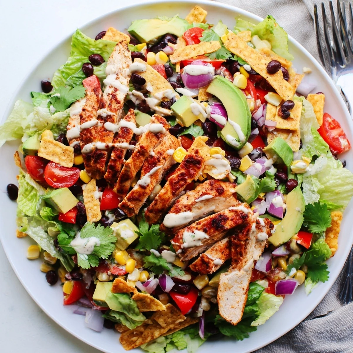 Fresh Southwestern chicken salad featuring juicy spiced grilled chicken atop a vibrant bed of vegetables, creamy avocado, and tangy yogurt lime dressing.