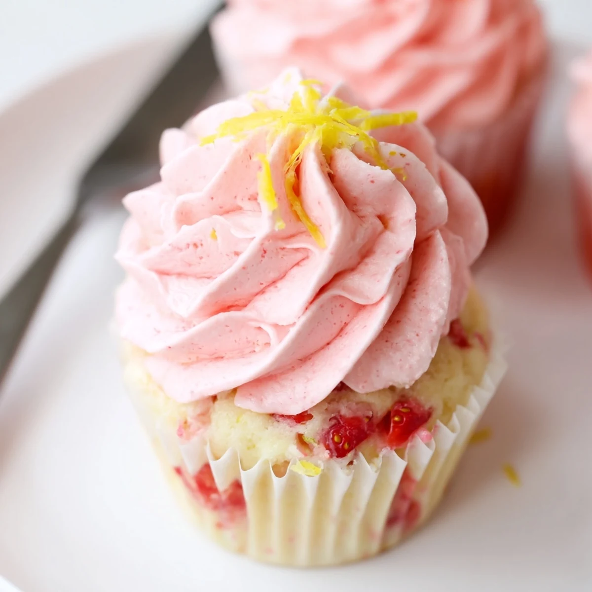 Freshly piped Strawberry Lemonade Cupcakes garnished with sliced strawberries and lemon