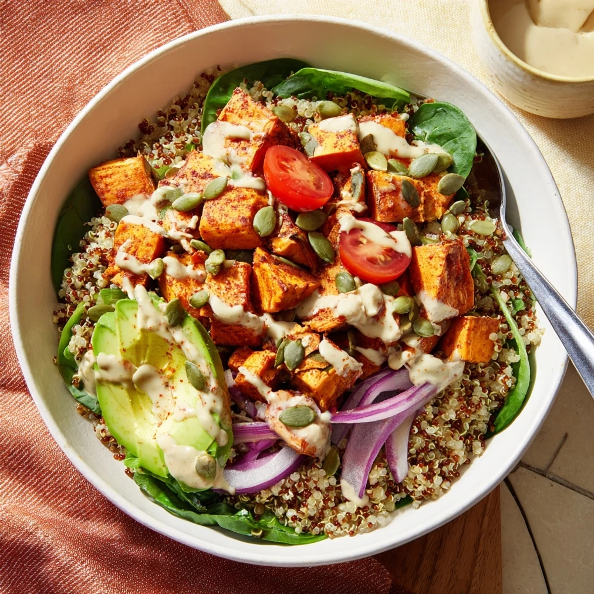Warm sweet potato bowl layered with fresh greens, sliced avocado, and zesty tahini sauce