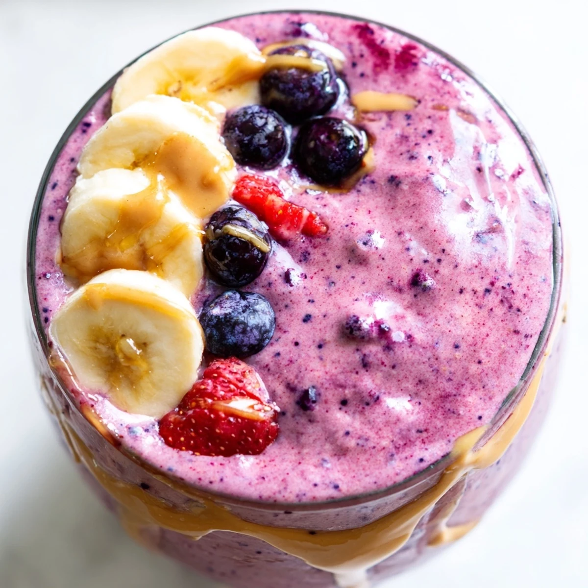 Thick purple peanut butter berry smoothie poured into a glass topped with fresh strawberries and a swirl of peanut butter