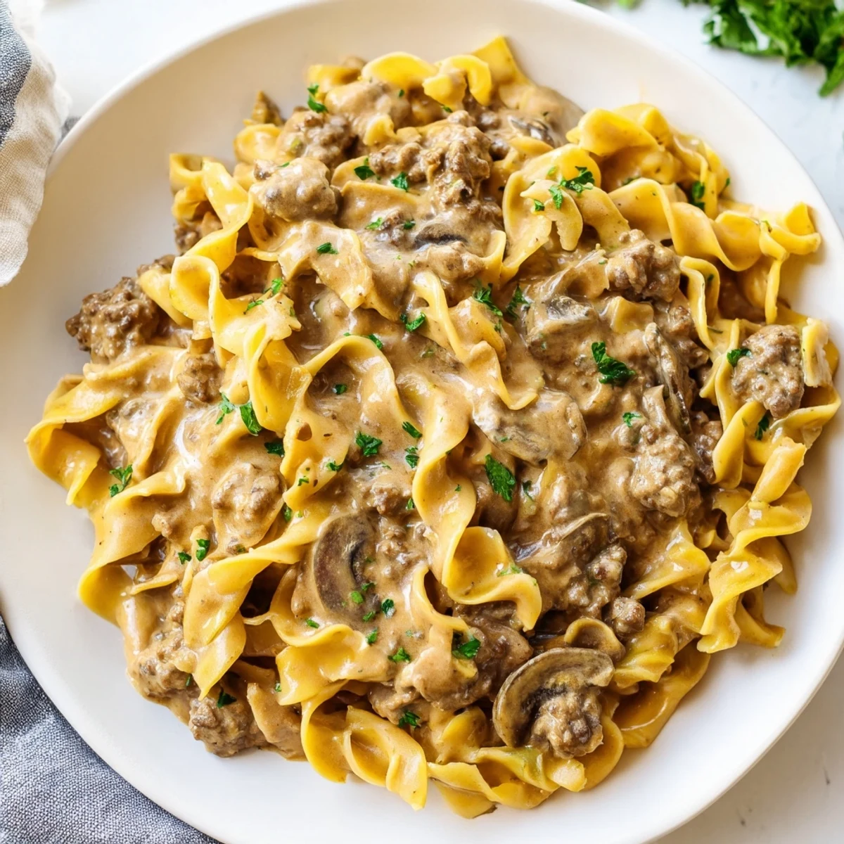 Warm bowl of hamburger stroganoff topped with chopped parsley beside buttery egg noodles
