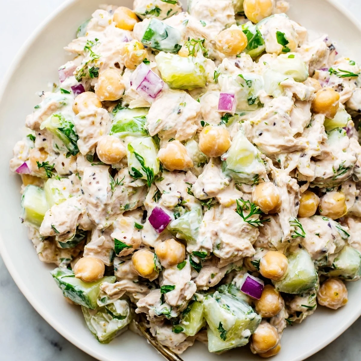 A bowl of creamy tuna chickpea cucumber salad topped with fresh parsley and cherry tomatoes