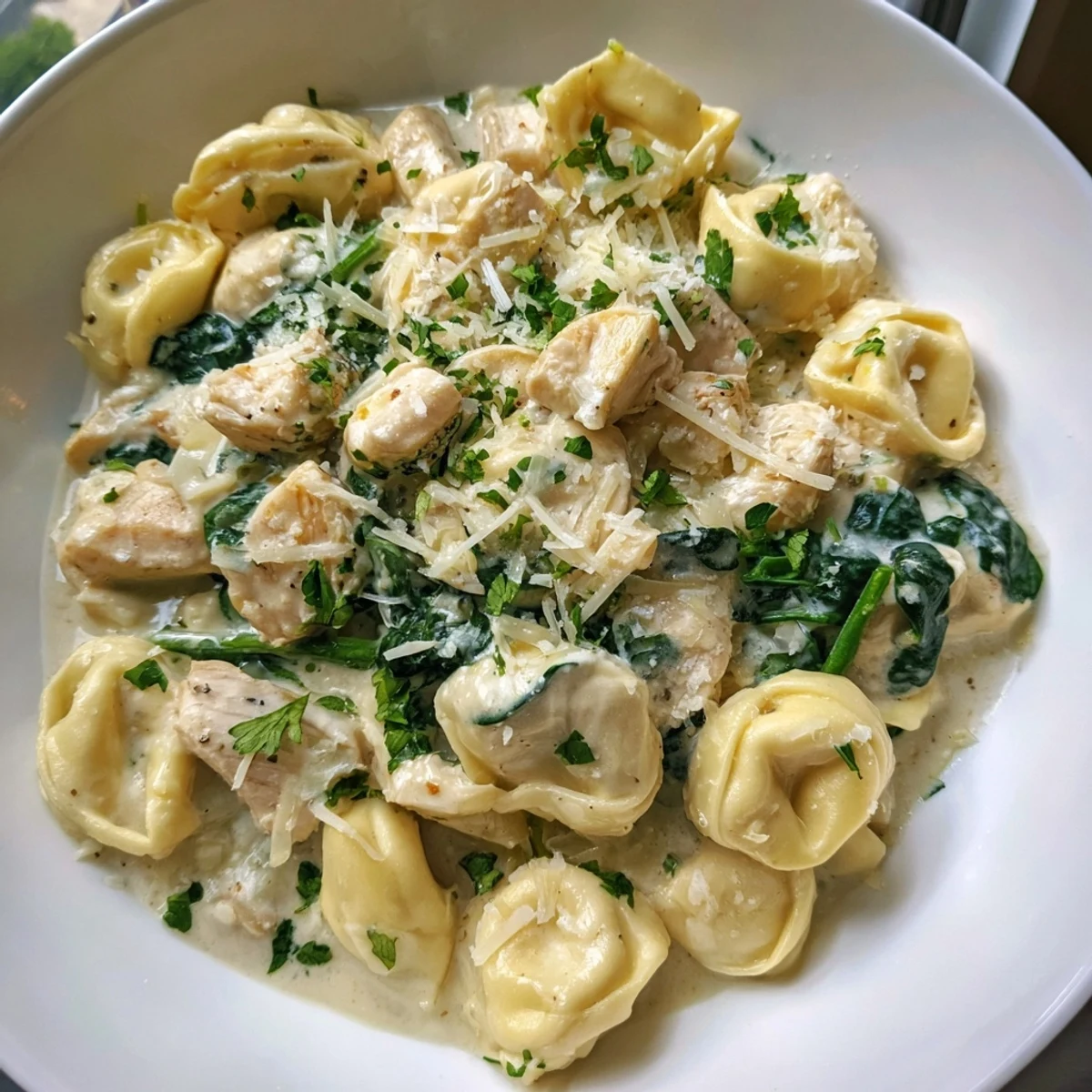 Steaming creamy garlic chicken tortellini with wilted spinach topped with fresh parsley