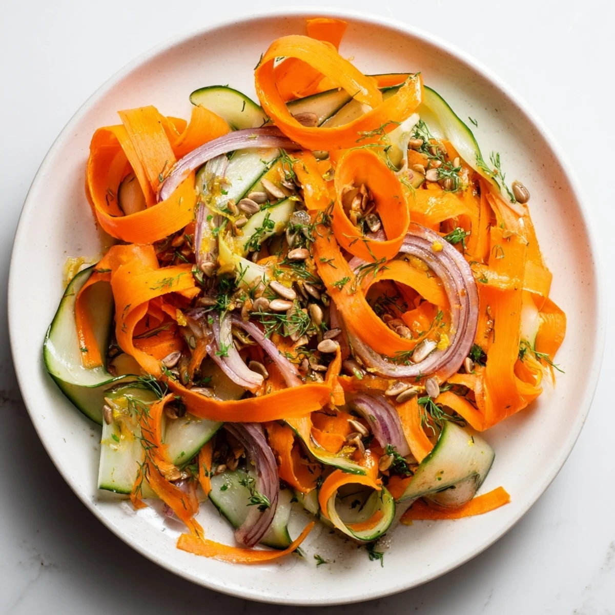 Fresh carrot ribbons in a bowl with cucumber, red onion, and citrus dressing  