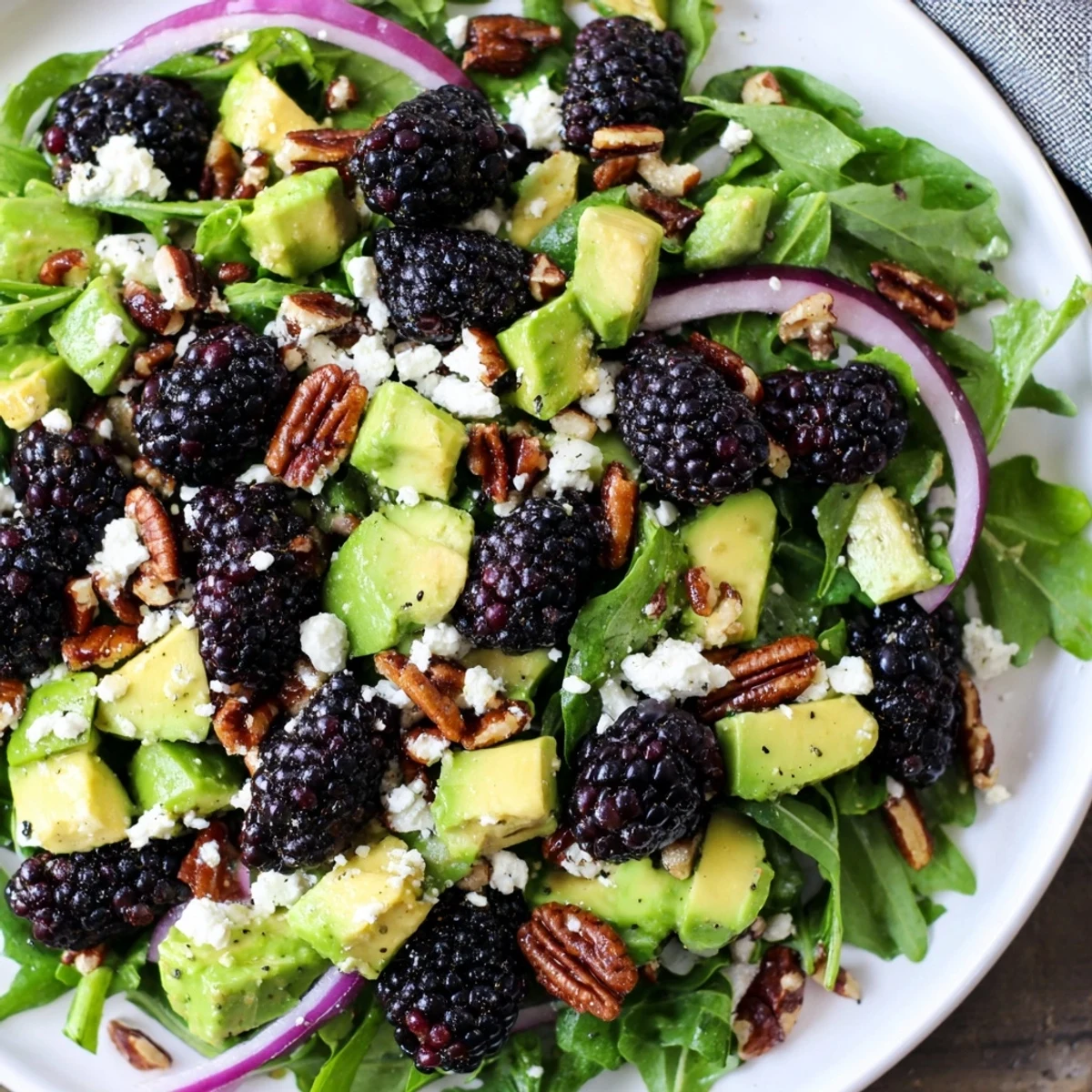 Colorful Blackberry Avocado Salad topped with feta, pecans, and red onion slices.  