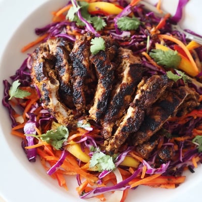 Grilled jerk chicken sliced over crisp colorful mango slaw with lime wedges